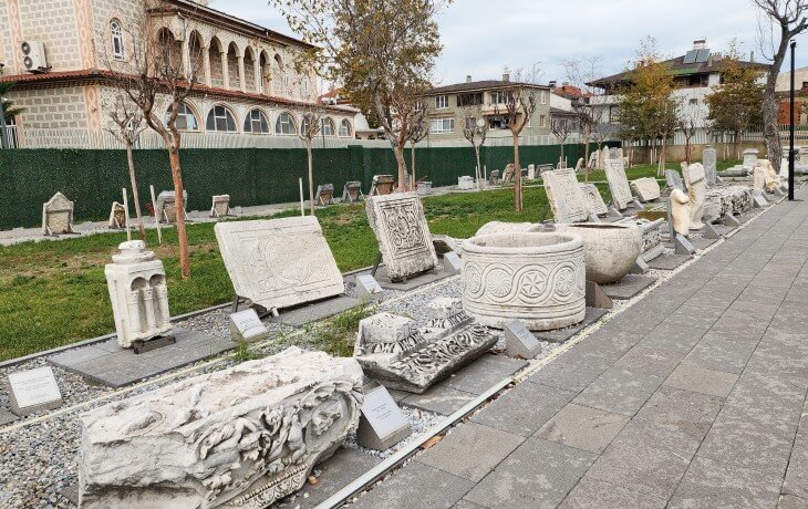 İznik Müzesi bahçesinde sergilenen Roma ve Bizans dönemine ait taş lahitler, mezar stelleri ve oyma mermer eserlerin açık hava düzenlemesini gösteren fotoğraf.